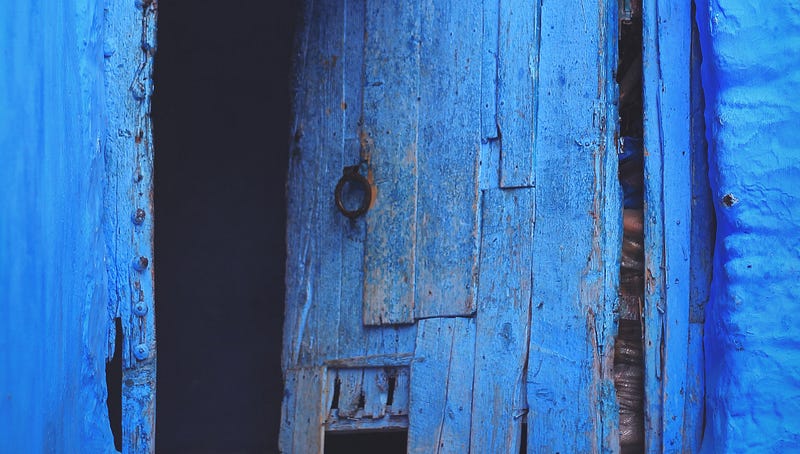 An old blue door slightly open, darkness inside