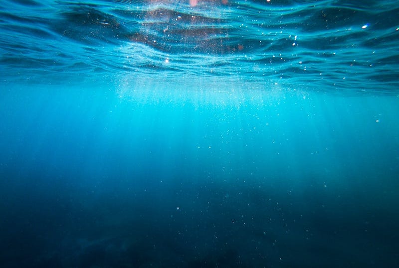 Under the surface of the sea, light rays shining in, beautiful clear water but you can feel the weight and the depth at the bottom